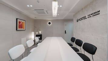 A conference room with a long table, chairs, a chandelier, a framed picture, and a wall sign for 'HOSTEL THE MEOMUM SEOUL JONGNO'.