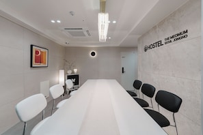 Een vergaderruimte met een lange tafel, stoelen, een kroonluchter, een ingelijste foto en een bord met de tekst 'HOSTEL THE MEOMUM SEOUL JONGNO'.