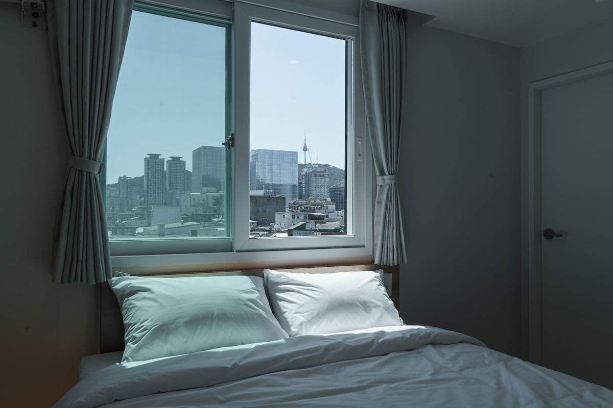 Een hotelkamer met een bed, gordijnen en een raam met uitzicht op de stad.