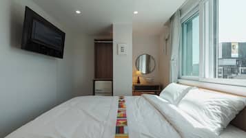A hotel room with a bed, a bedside table with a lamp, a mirror, a wardrobe, and a TV mounted on the wall.