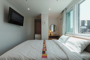 Een hotelkamer met een bed, nachtkastje met een lamp, spiegel, kledingkast en een aan de muur bevestigde televisie.