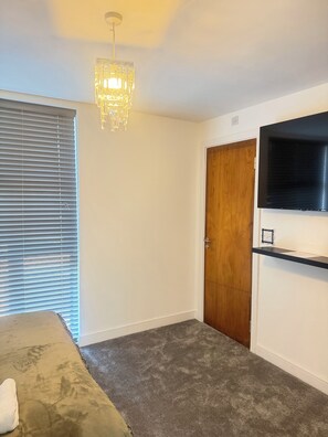 A room with a bed, a wooden door, a mounted TV, and a hanging light fixture. - Luxury 5 bedrooms with 5 bathrooms (Birmingham)