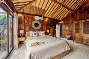 Ein geräumiges Schlafzimmer mit einem großen Bett, Holzwänden, einem Deckenventilator und Blick durch eine Glastür.