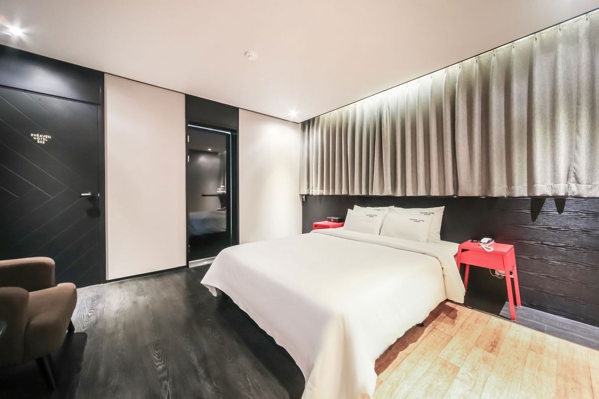 Un dormitorio moderno con una cama grande, una mesita de noche roja, una silla y un suelo de madera oscura.