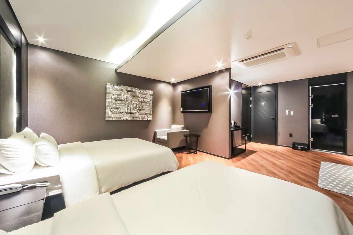 Habitación de hotel con cama, mesita de noche, una silla, escritorio, televisión de pantalla plana y una obra de arte colgada en la pared.