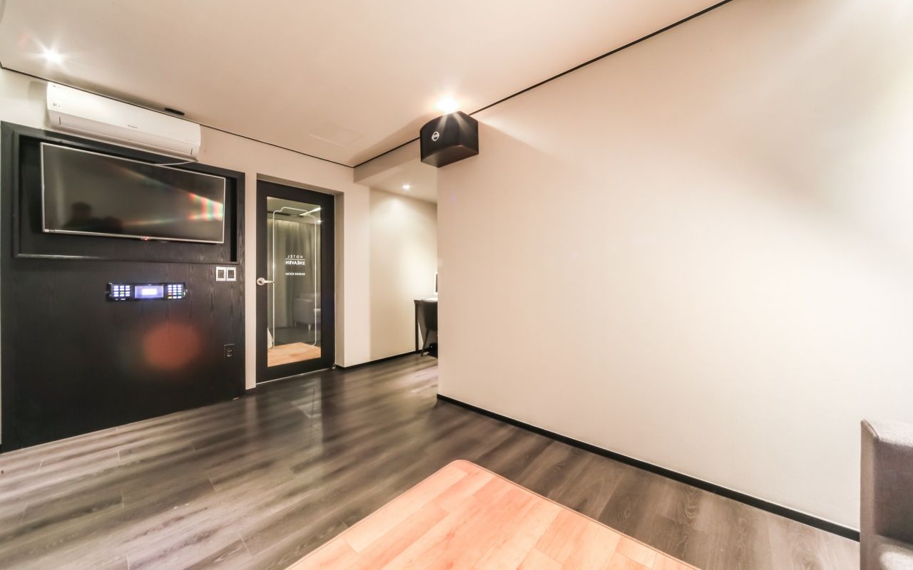 Um corredor moderno com piso de madeira, uma porta preta com visor digital e luminária fixada na parede.