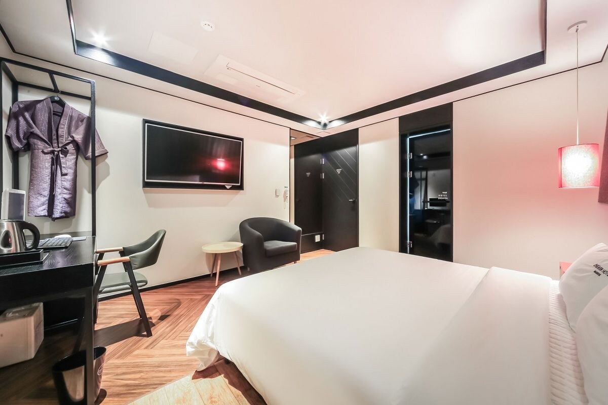 Una habitación de hotel con una cama, un escritorio con una silla, un televisor y un armario.