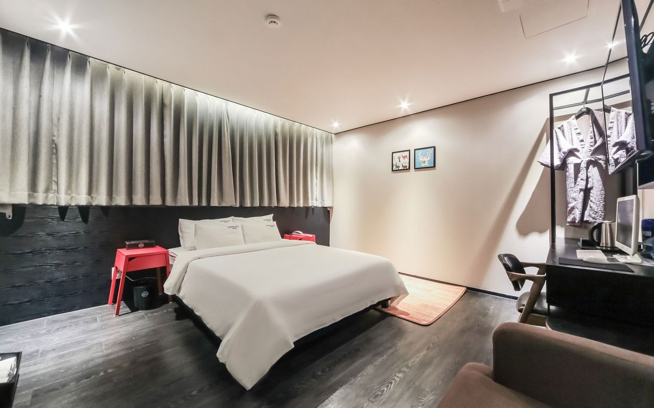 Un dormitorio moderno con una cama, una mesita de noche roja, un escritorio con una silla y un armario.