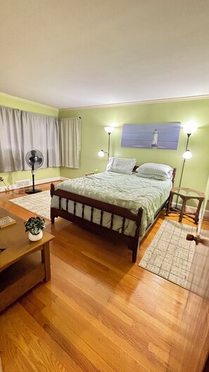 A bedroom with a wooden bed, a nightstand, a bedside lamp, a wall-mounted picture, and a floor lamp. - Family-Friendly 3BR with Private B-Ball Court & Patio (Statesville)