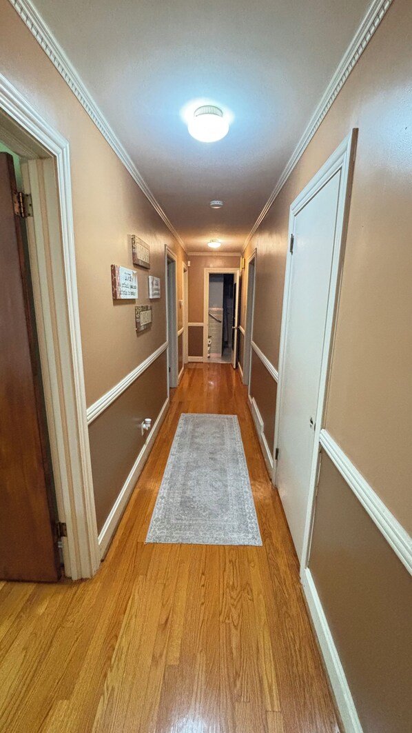 A hallway with wooden floors, a gray rug, and white trim on the walls.