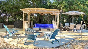 An outdoor patio with a wooden pergola, blue cushioned seating, and a table with chairs. - Family-Friendly 3BR with Private B-Ball Court & Patio (Statesville)