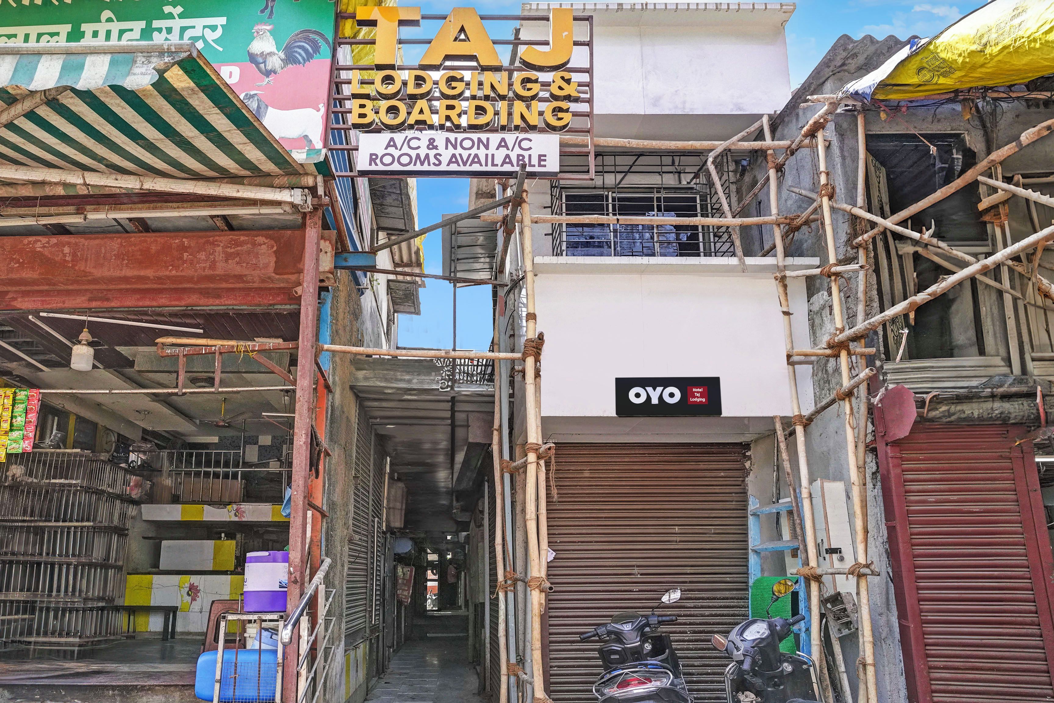 A narrow alley with a sign for Taj Lodging & Boarding offering A/C and non-A/C rooms.