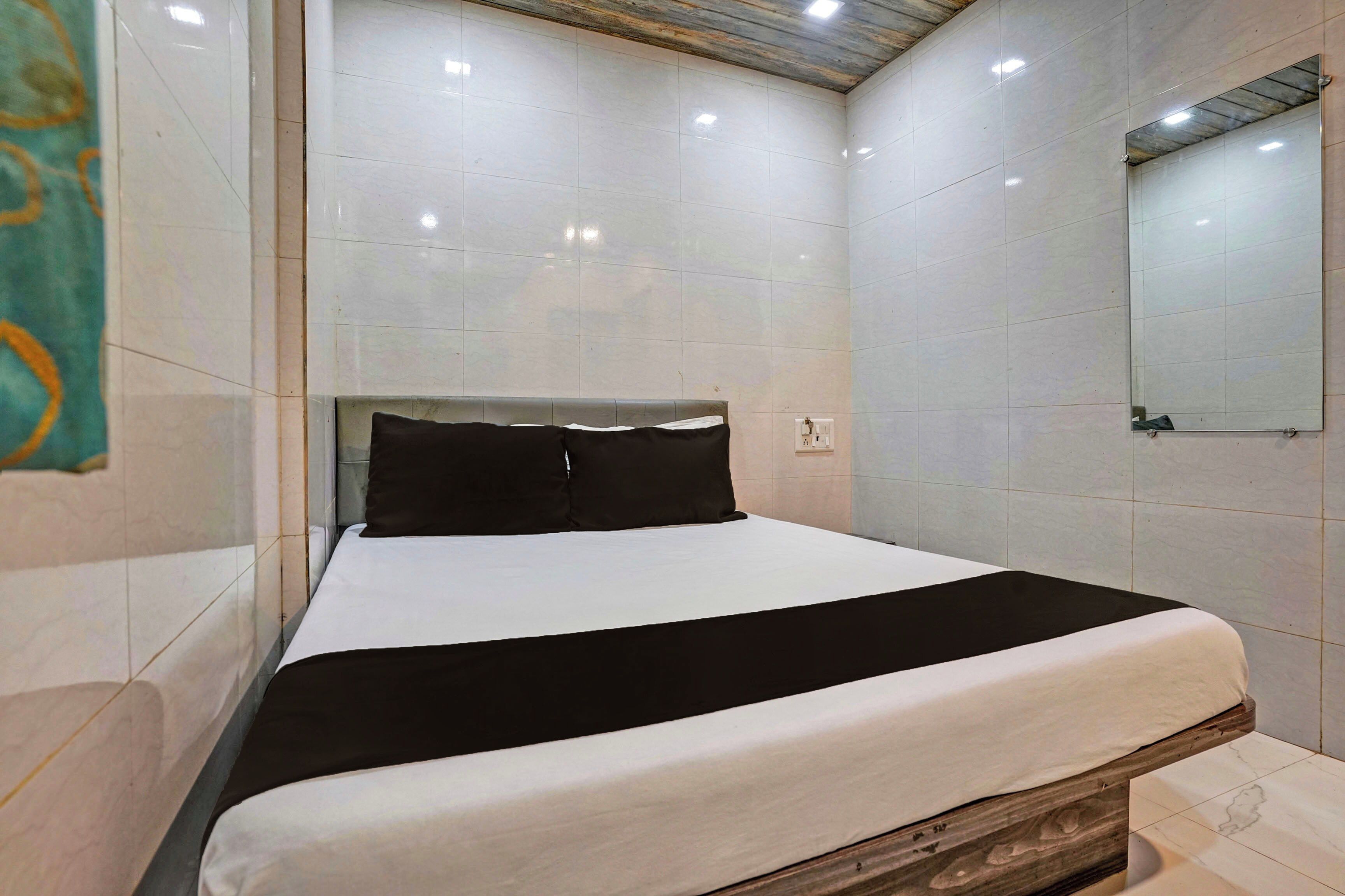 Quarto de hotel com cama, cabeceira de madeira, espelho e paredes revestidas de azulejos.