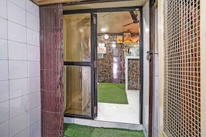 Entrada de un hotel con puerta de vidrio, un cartel de hora de salida y un pequeño espacio exterior con césped artificial.