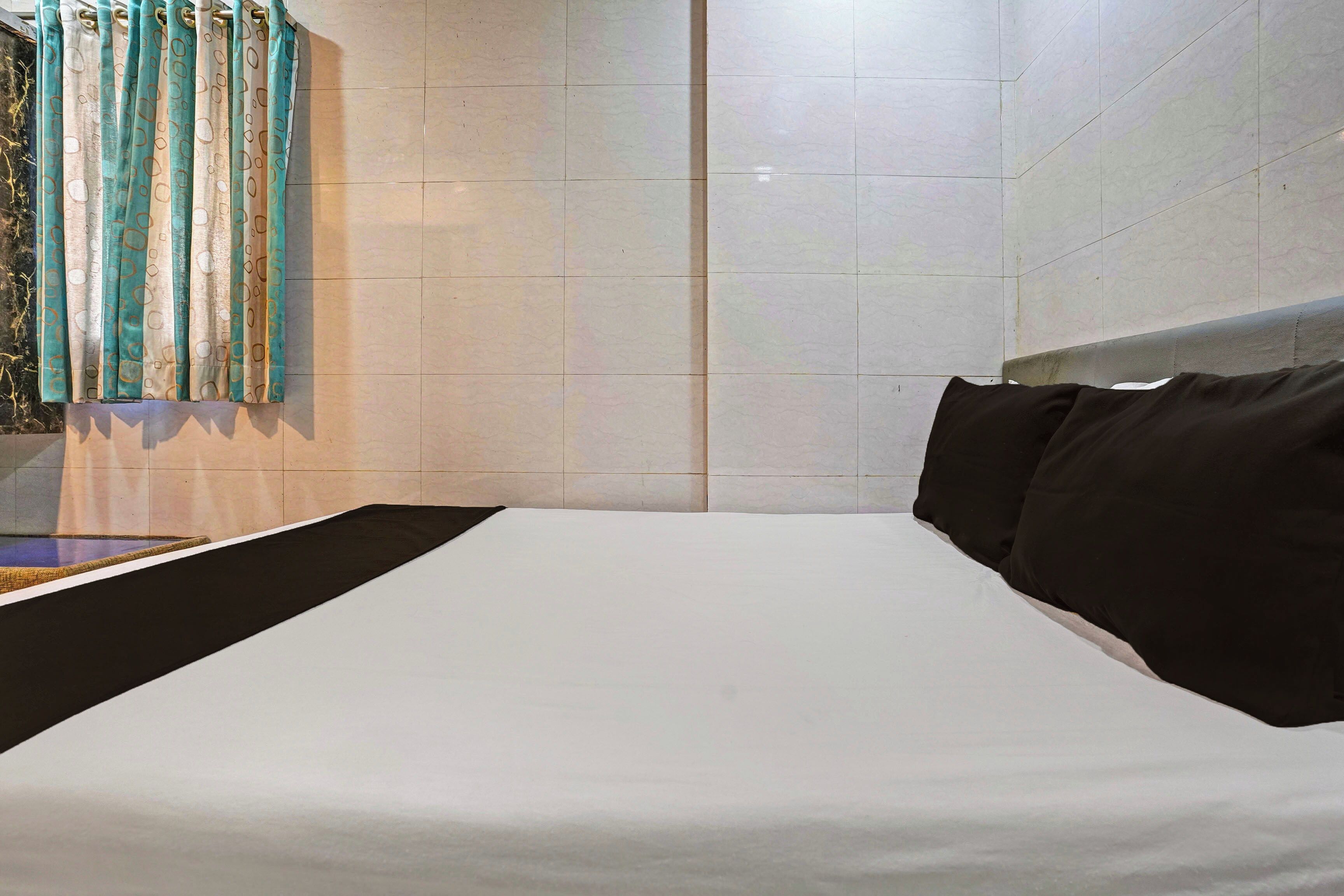A hotel room with a bed, a window with curtains, and a tiled wall.