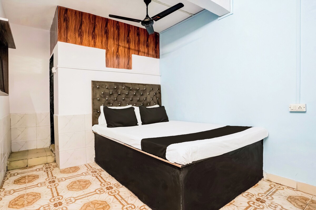 A bedroom with a bed, a ceiling fan, a wooden panel above the bed, and patterned floor tiles.