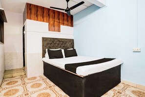 A bedroom with a bed, a ceiling fan, a wooden panel above the bed, and patterned floor tiles. - Hotel O Vira Palace (Mumbai)