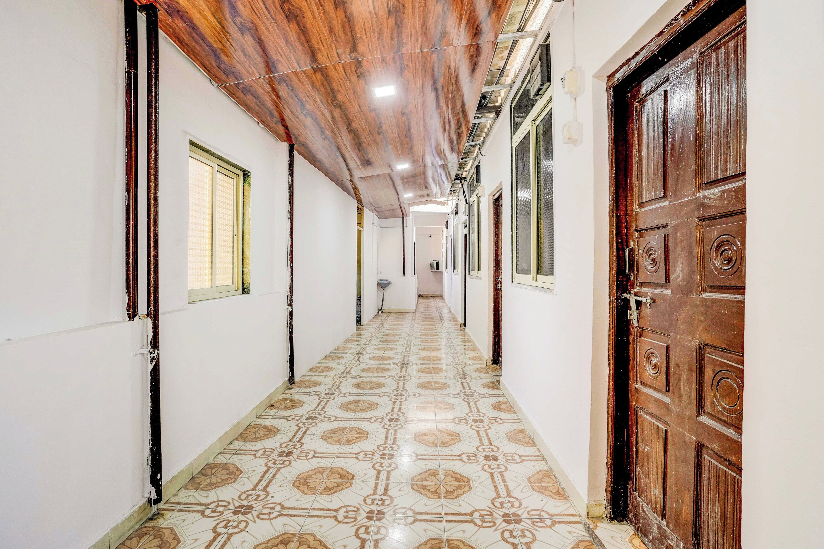 A corridor with patterned floor tiles, wooden doors, and windows with blinds.