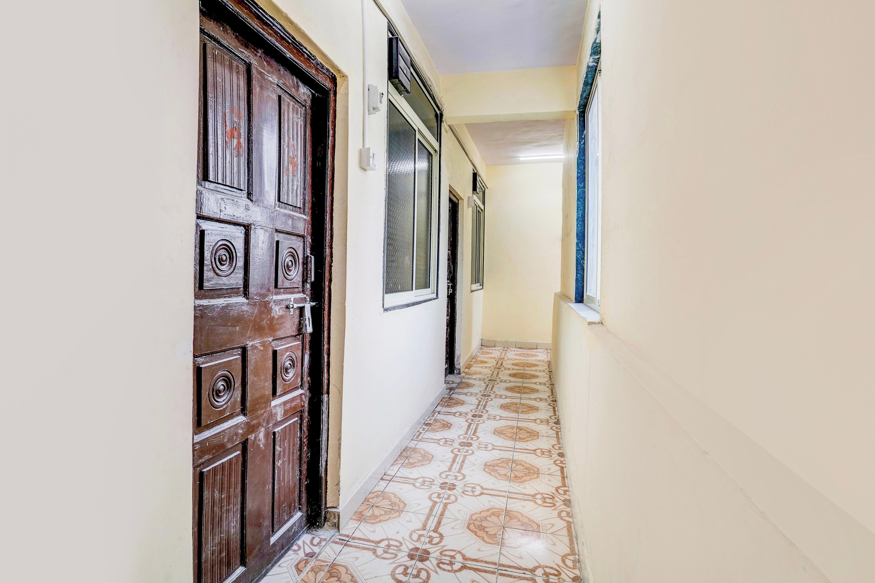 A narrow hallway with a wooden door and patterned floor tiles.