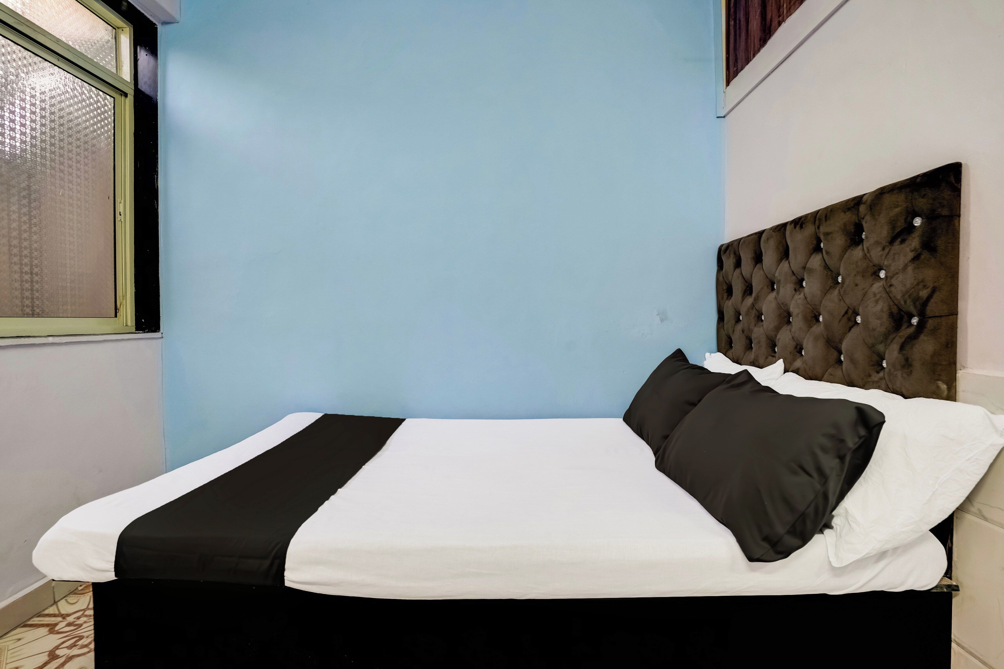 Una cama con cabecera capitonada, ropa de cama blanca y negra, y una ventana con persiana estampada.