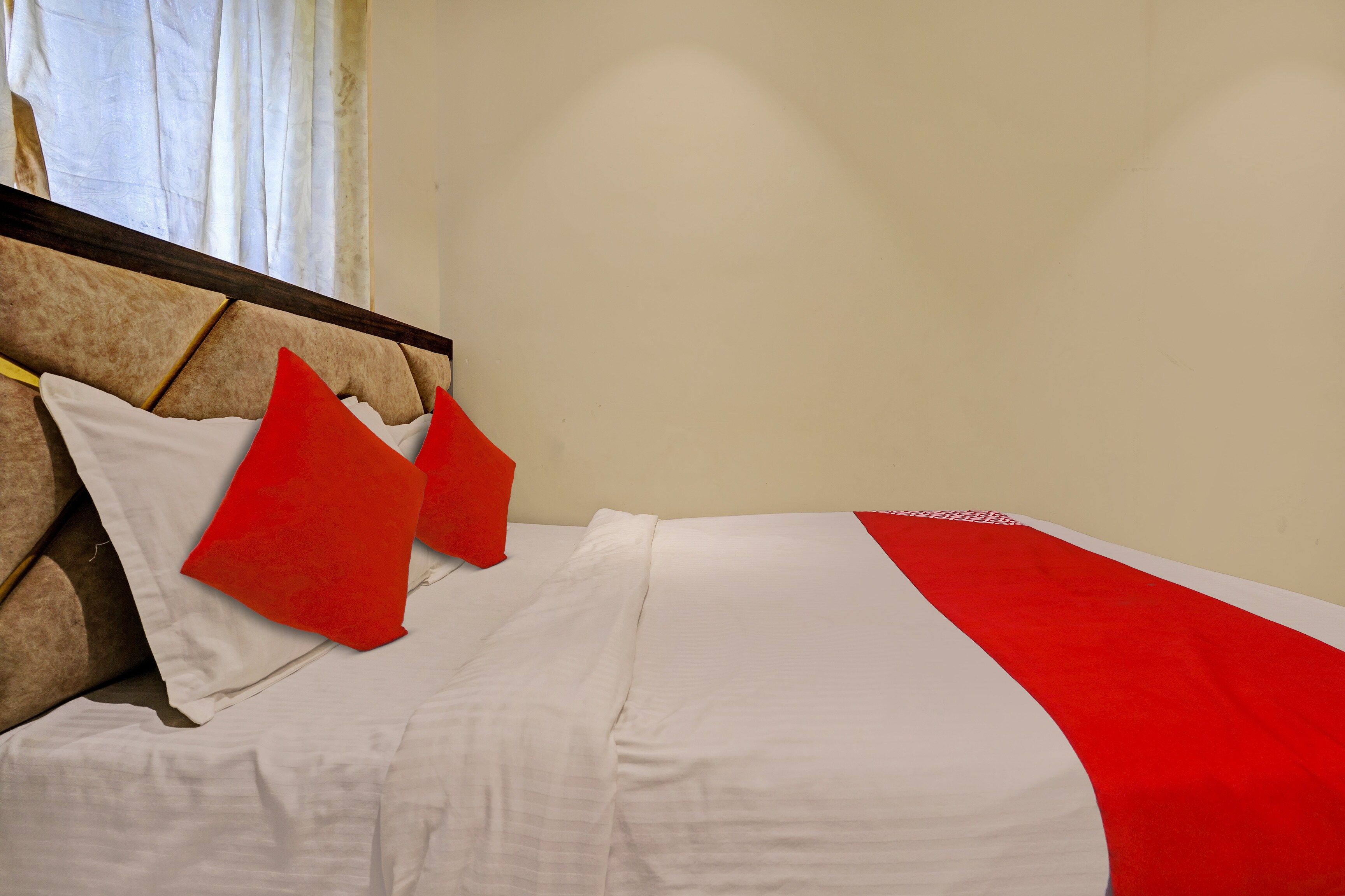 Una cama con ropa blanca y almohadas rojas, un cabecero de madera y una colcha a rayas rojas y blancas.