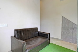 Una habitación con un sofá de cuero marrón oscuro, una pared blanca, una alfombra verde y una puerta con manija de metal.