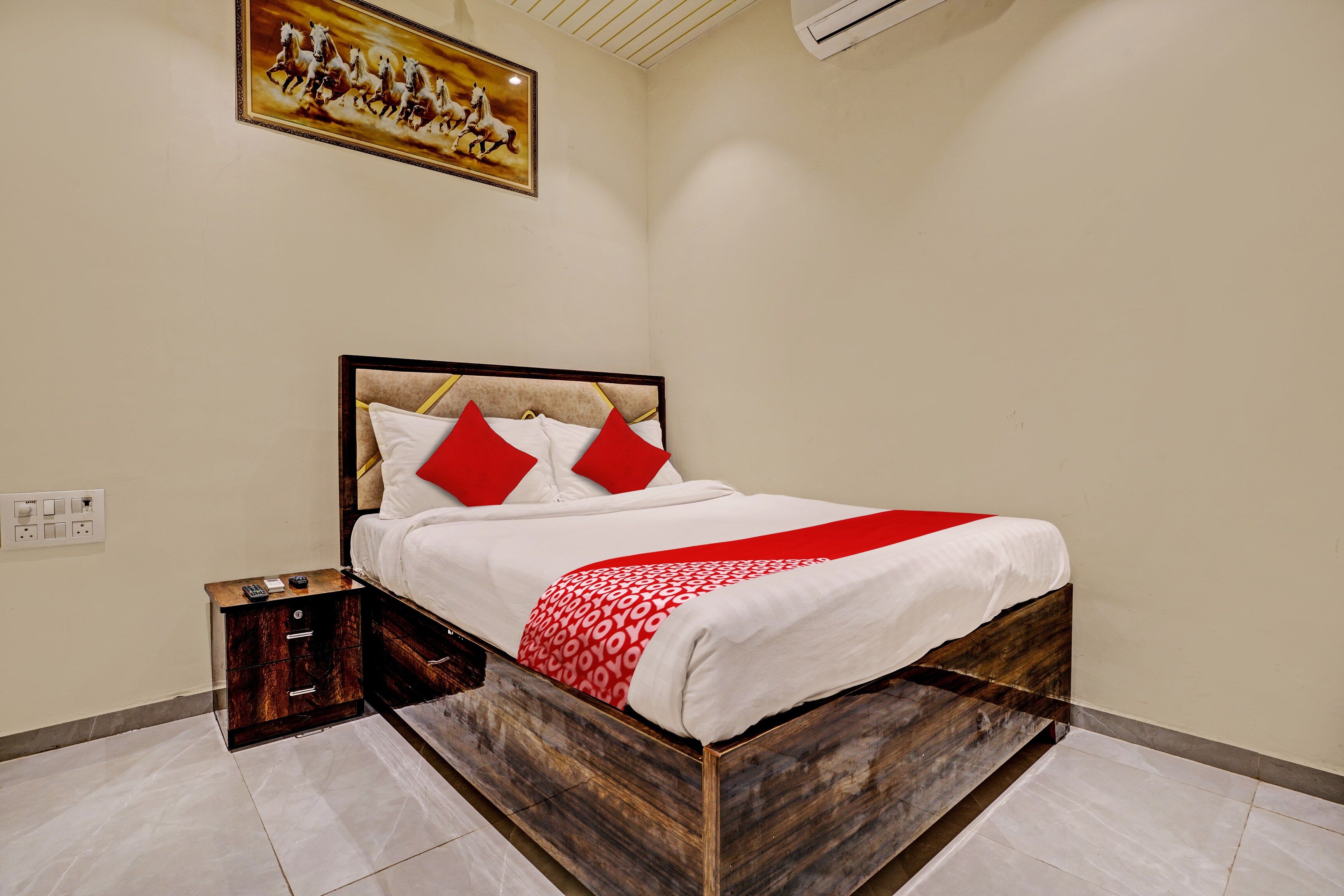 Een opgemaakt bed met een houten frame, witte beddengoed en rode kussens.