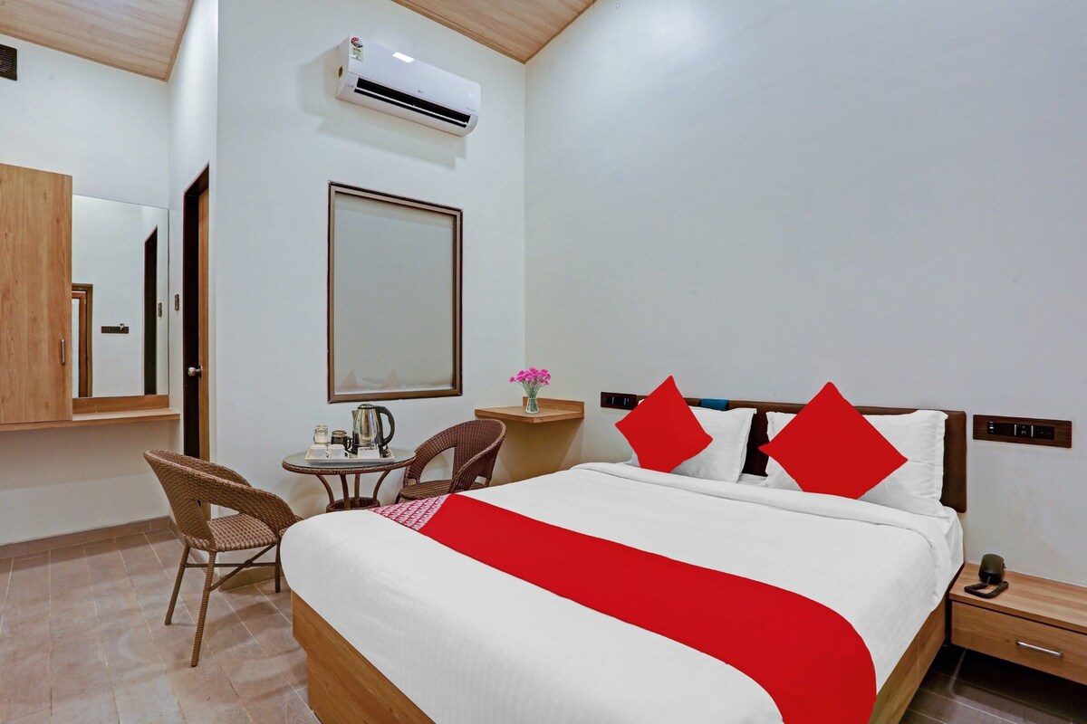 Quarto de hotel com uma cama, uma cadeira, uma mesinha com chaleira e um espelho.