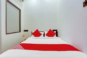 Uma cama de solteiro com um edredom branco e vermelho, duas almofadas vermelhas e um pequeno vaso com flores sobre uma mesa de cabeceira.