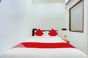 Quarto de hotel com cama, mesa de cabeceira, um vaso com flores e ar condicionado fixado na parede.