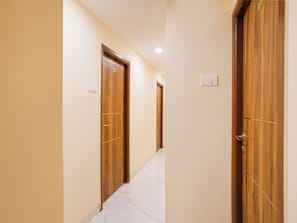 Un pasillo con puertas de madera, suelo de baldosas y un interruptor de luz en la pared.