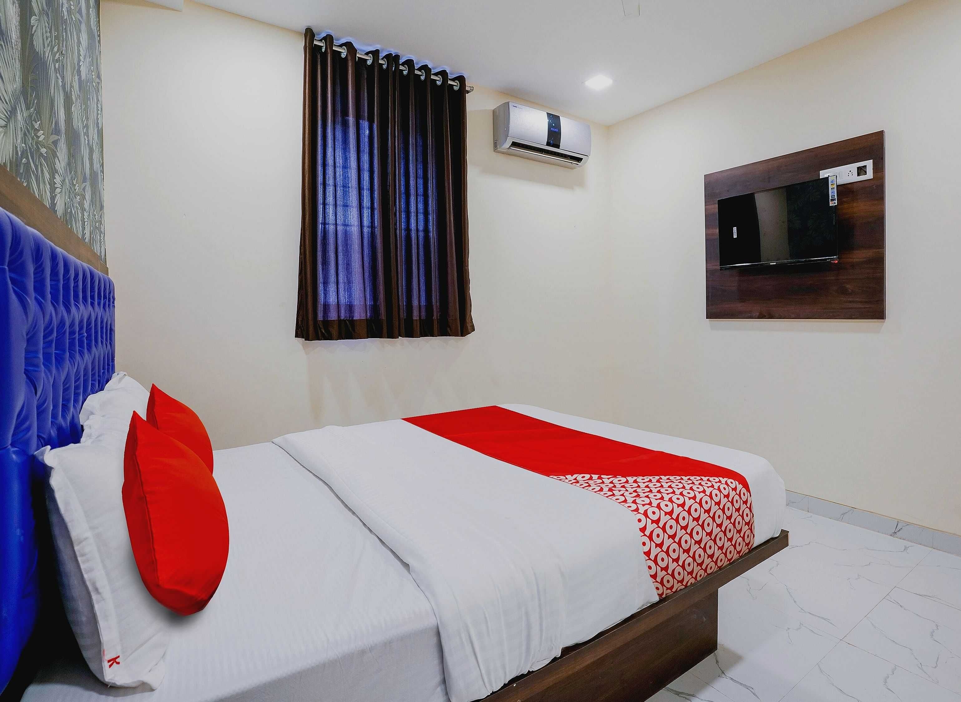 Habitación de hotel con cama, aire acondicionado de pared, ventana con cortinas y televisor de pantalla plana.
