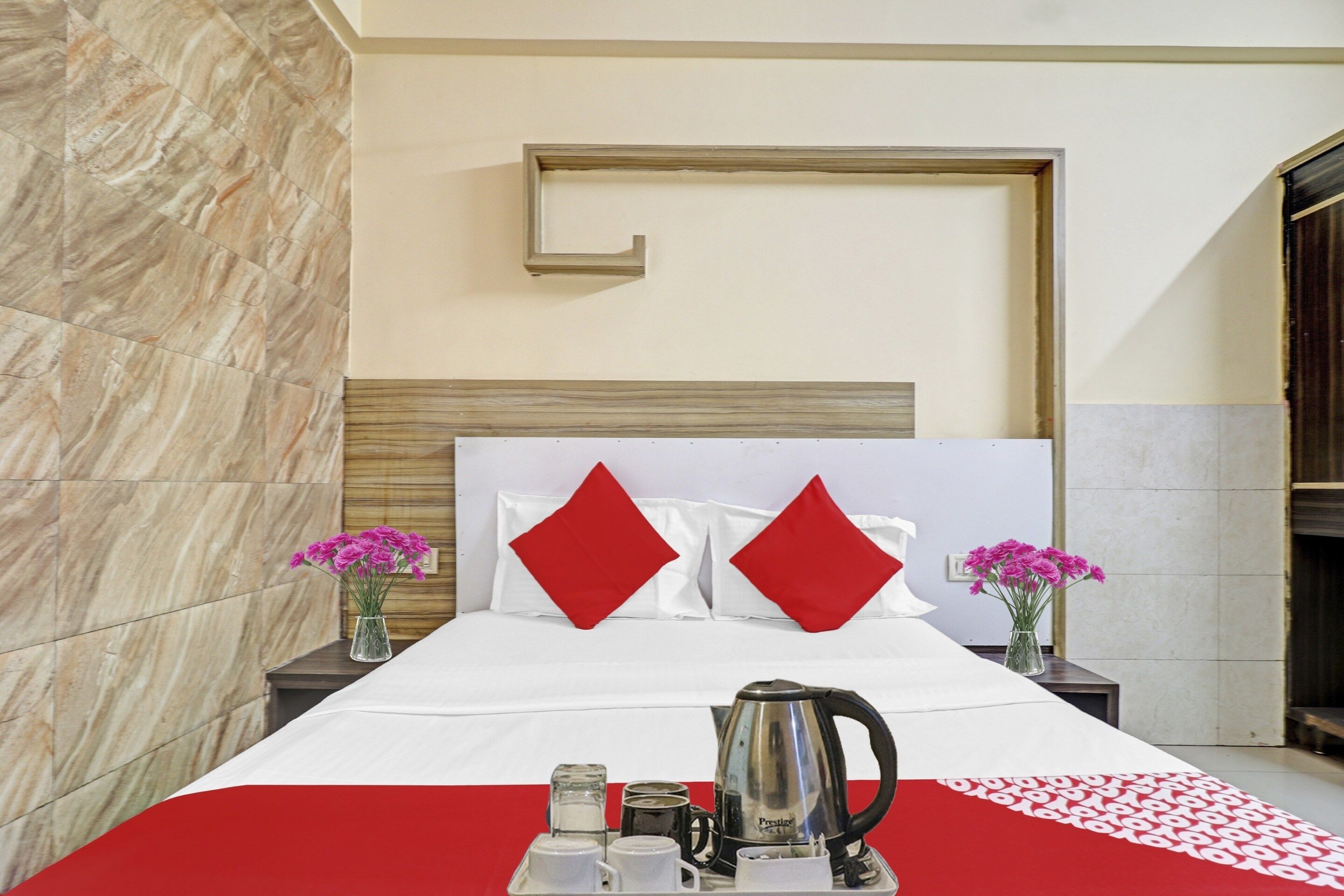 A hotel room with a bed, two nightstands, a red and white checkered table runner, a coffee maker, and two vases with flowers.