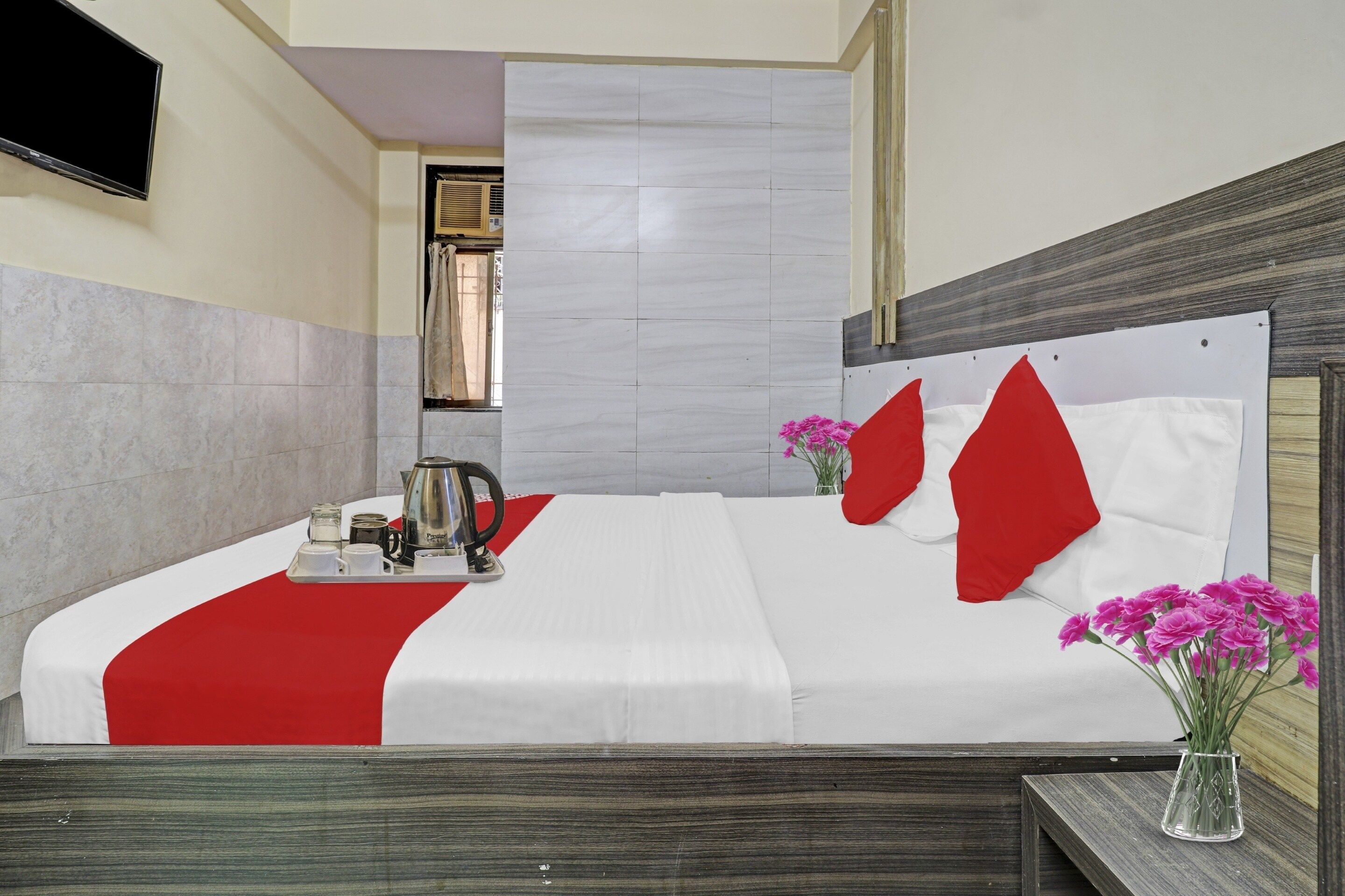A hotel room with a bed, a bedside table with a vase of flowers, and a window with curtains.