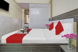 A hotel room with a bed, a bedside table with a vase of flowers, and a window with curtains.