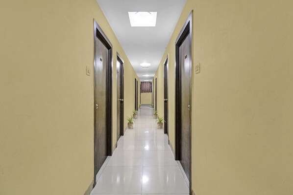 A hotel corridor with doors on both sides, a tiled floor, and potted plants along the walkway.
