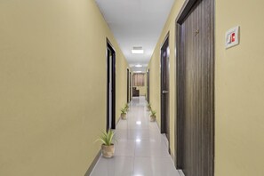 Un couloir avec des portes de chaque côté, des plantes en pot et un détecteur d’incendie au mur.