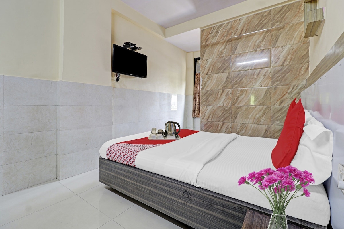 Une chambre d’hôtel avec un lit, un téléviseur à écran plat fixé au mur et un vase de fleurs sur la table de chevet.