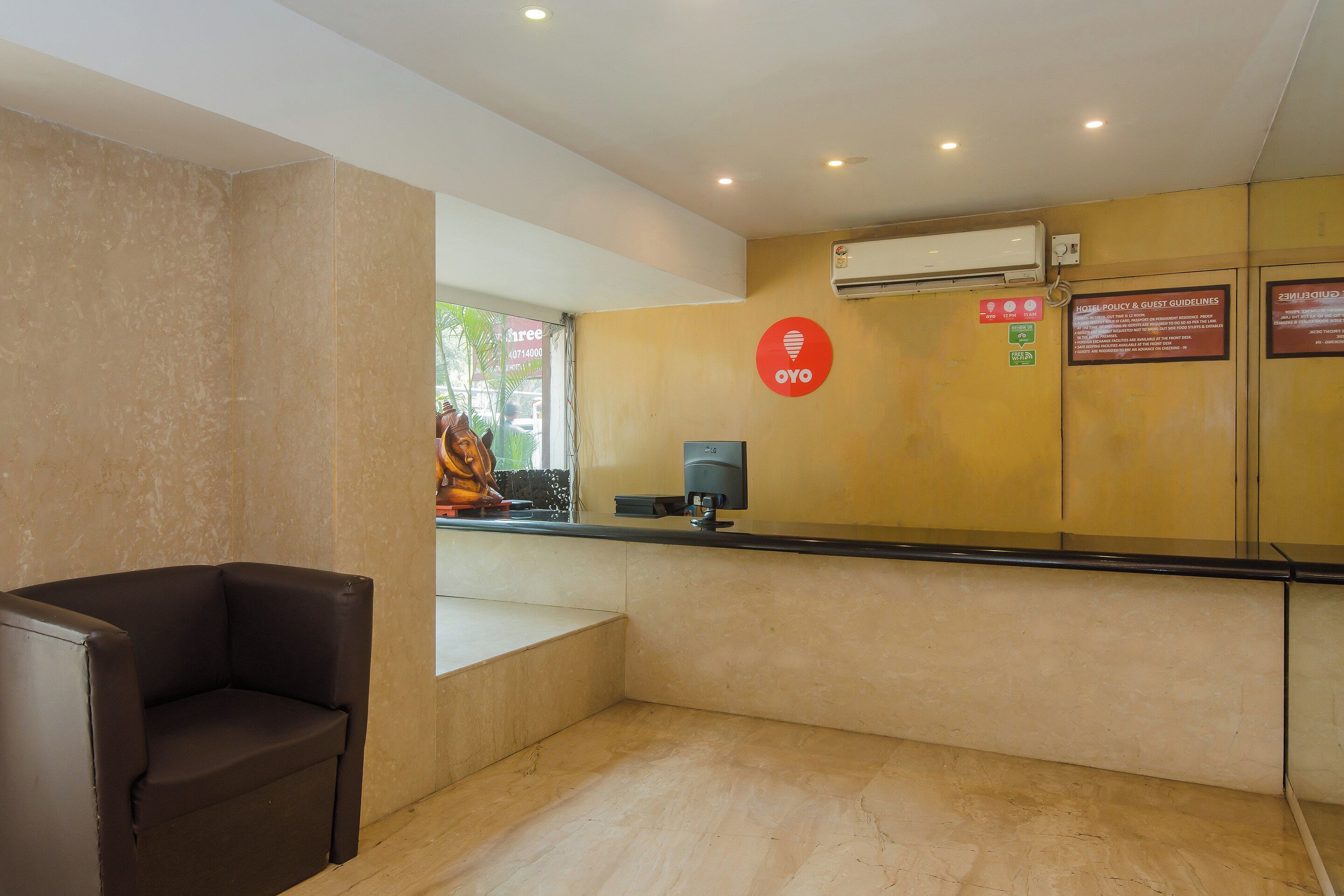 Zona de recepción de hotel con una silla de cuero marrón, un mostrador de recepción y un aire acondicionado instalado en la pared.