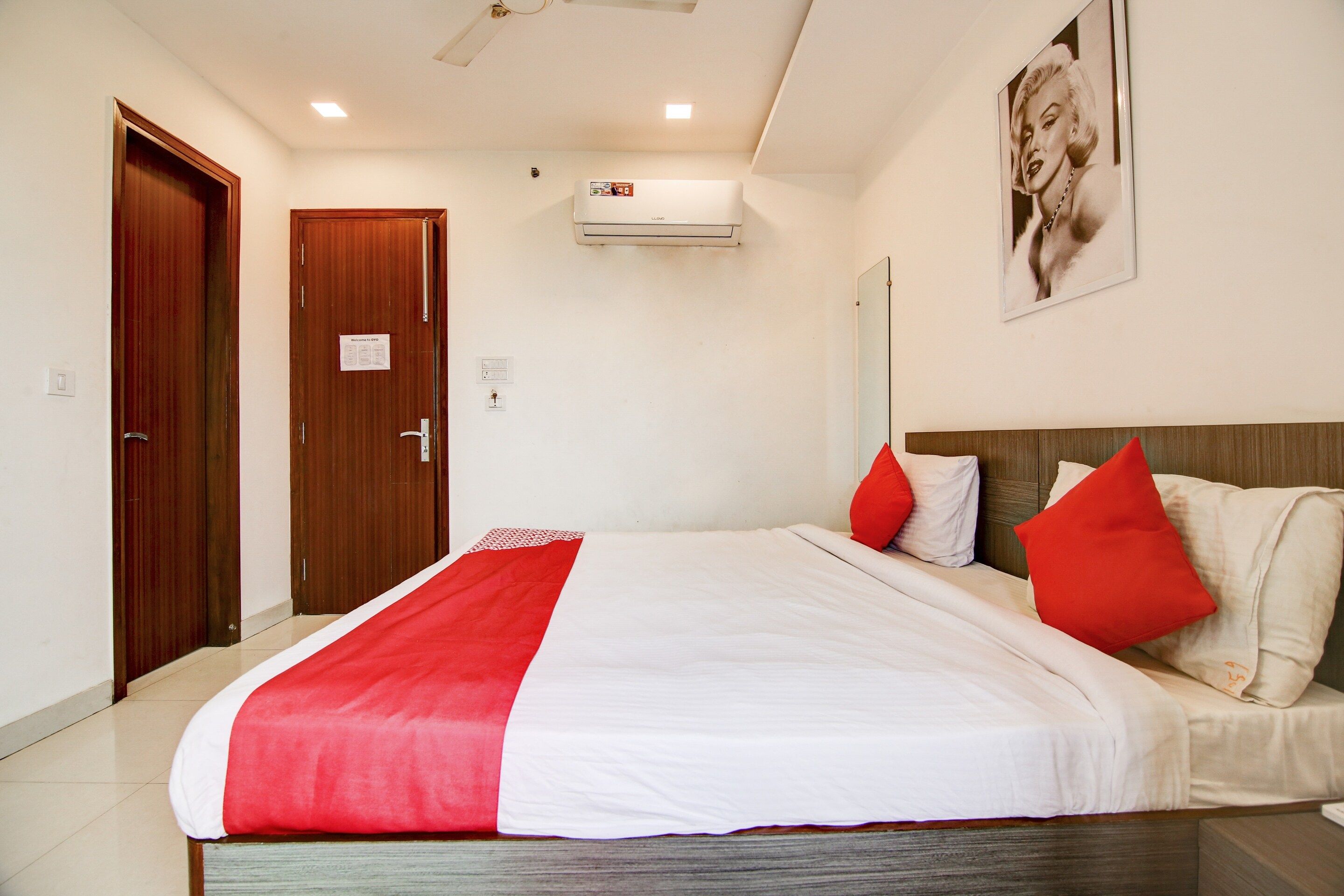 Una habitación de hotel con una cama, una puerta de madera, un equipo de aire acondicionado y un cartel en la pared.
