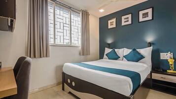 Habitació d'hotel amb un llit, escriptori, cadira, finestra amb cortines, ventilador de sostre i llums penjades a la paret.
