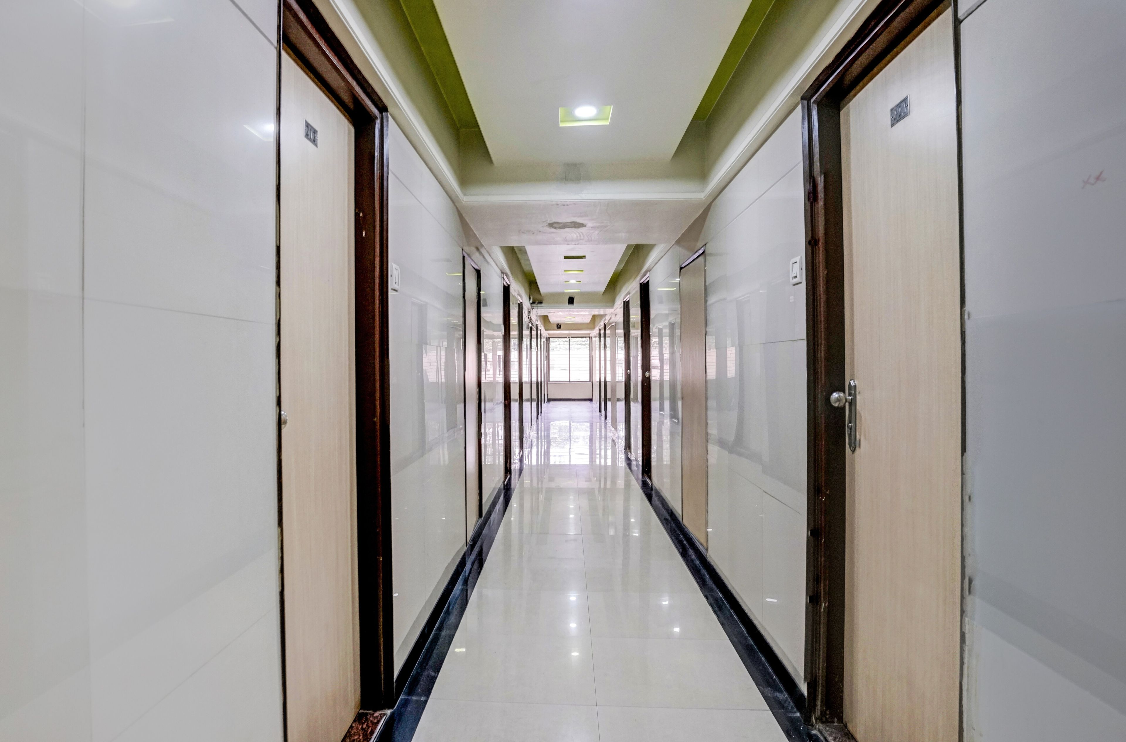 A long, narrow hotel corridor with doors on both sides, a tiled floor, and a ceiling with recessed lighting.