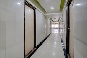 A long, narrow hotel corridor with doors on both sides, a tiled floor, and recessed ceiling lighting. - Collection O Guru Heritage Kalamboli (Panvel)