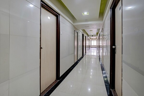 A long, narrow hotel corridor with doors on both sides, a tiled floor, and recessed ceiling lighting.