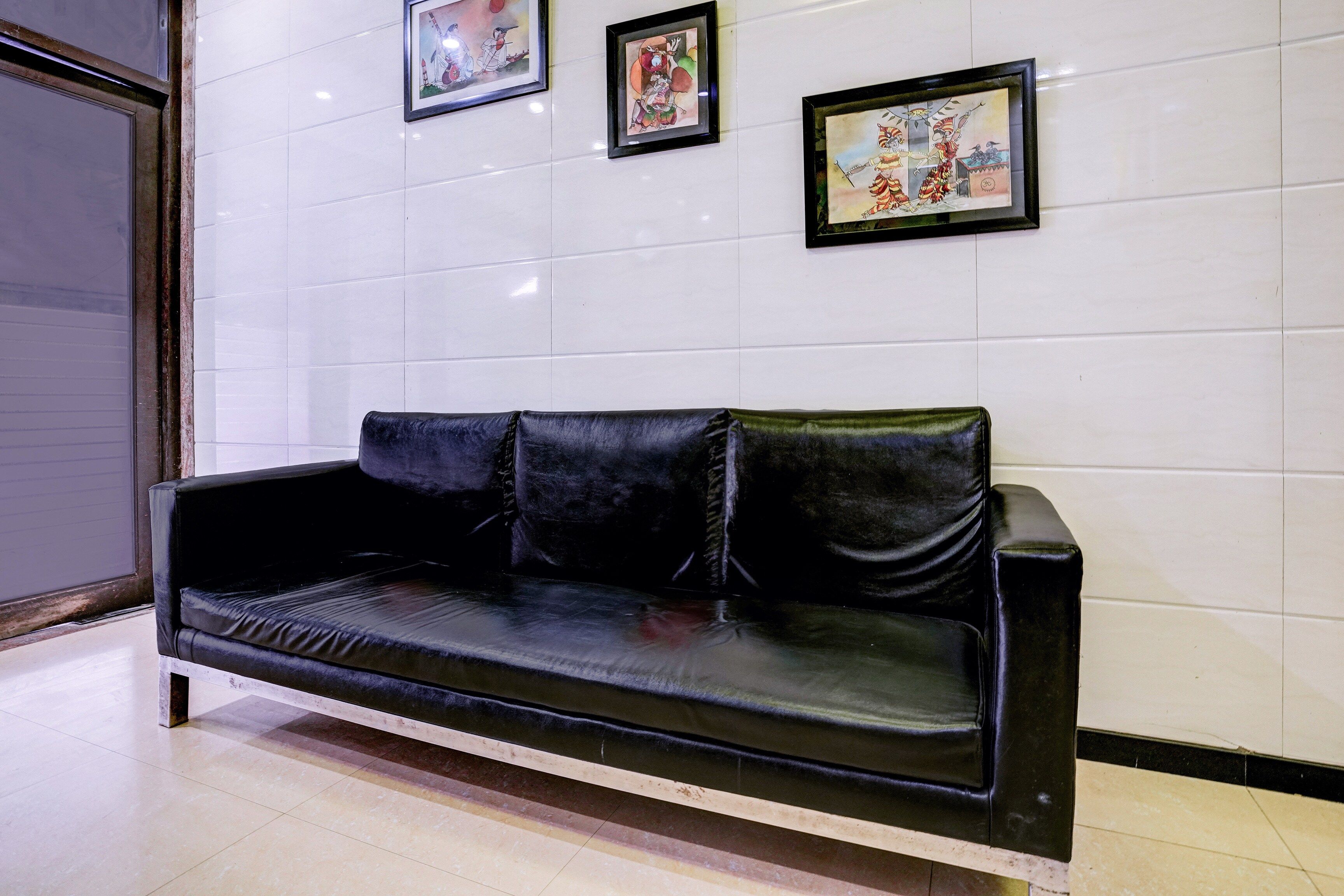 A black leather sofa against a white tiled wall with three framed artworks above it.