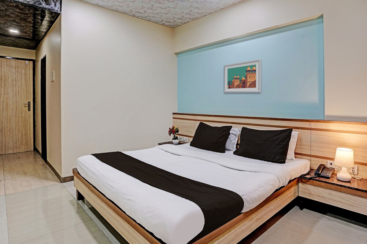 A hotel room with a bed, a nightstand with a lamp, a framed picture on the wall, and a door to the left.