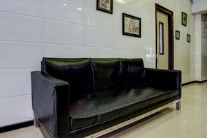 A black leather sofa against a white tiled wall with framed artwork.