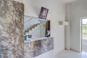 Un mostrador de recepción con una pared de mármol, un cuadro enmarcado encima y una escalera que sube a un nivel superior.