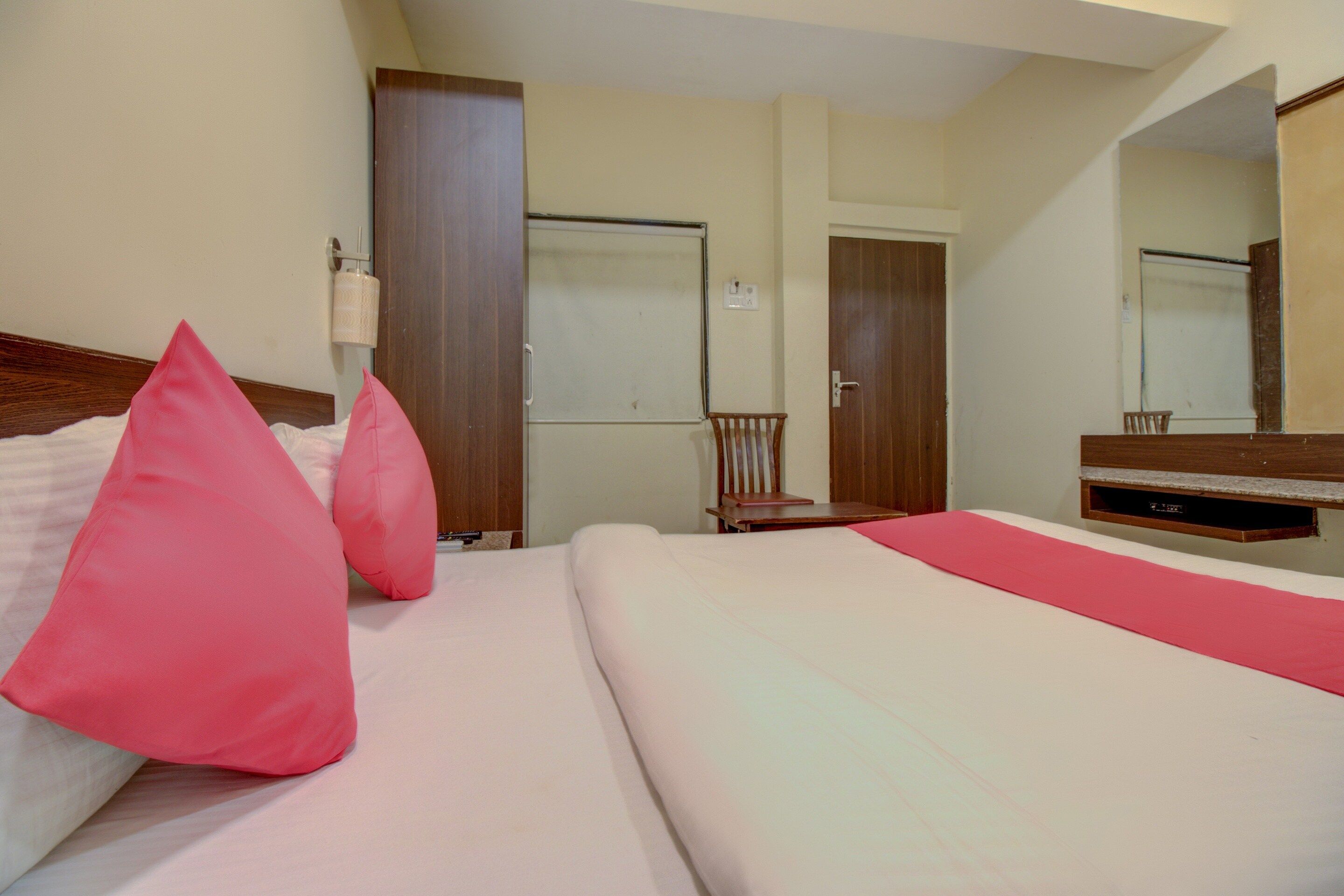 Una habitación de hotel con cama, almohadas, una silla, un escritorio y un espejo.