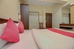 Una habitación de hotel con cama, almohadas, una silla, un escritorio y un espejo.